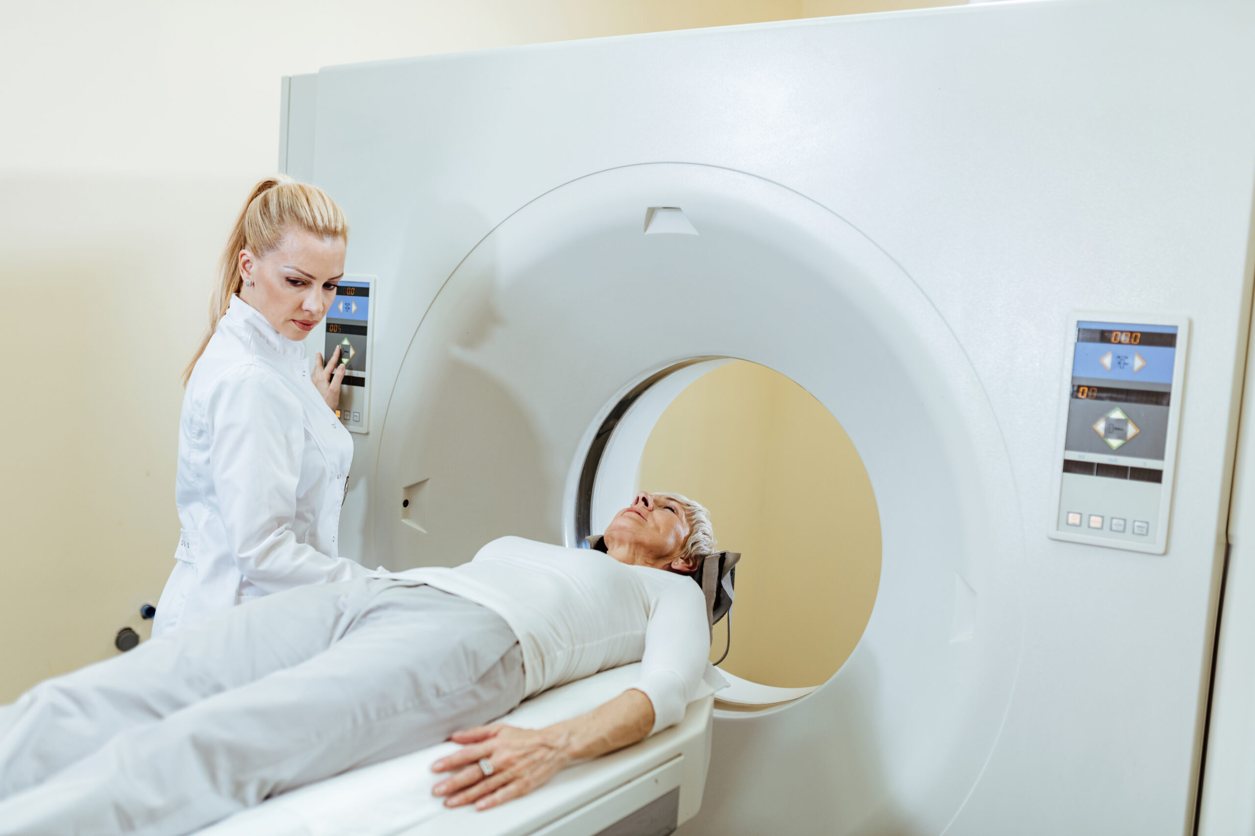 Female medical technician and mature patient during CT scan procedure in examination room at the hospital.